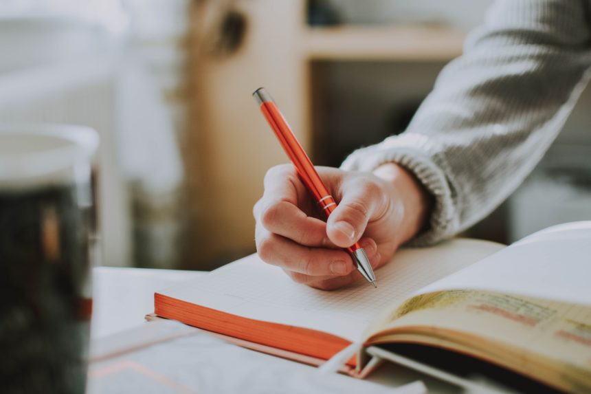 person holding orange pen e1565673083266
