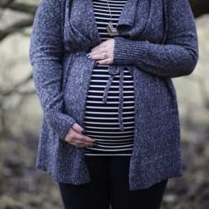 A pregnant woman wearing purple blazer holding her baby bump to celebrate pregnancy