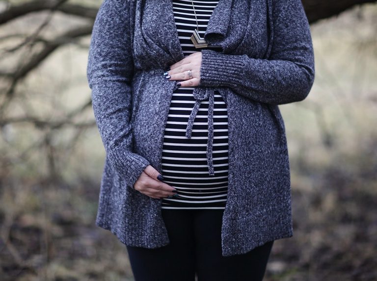 A pregnant woman wearing purple blazer holding her baby bump to celebrate pregnancy