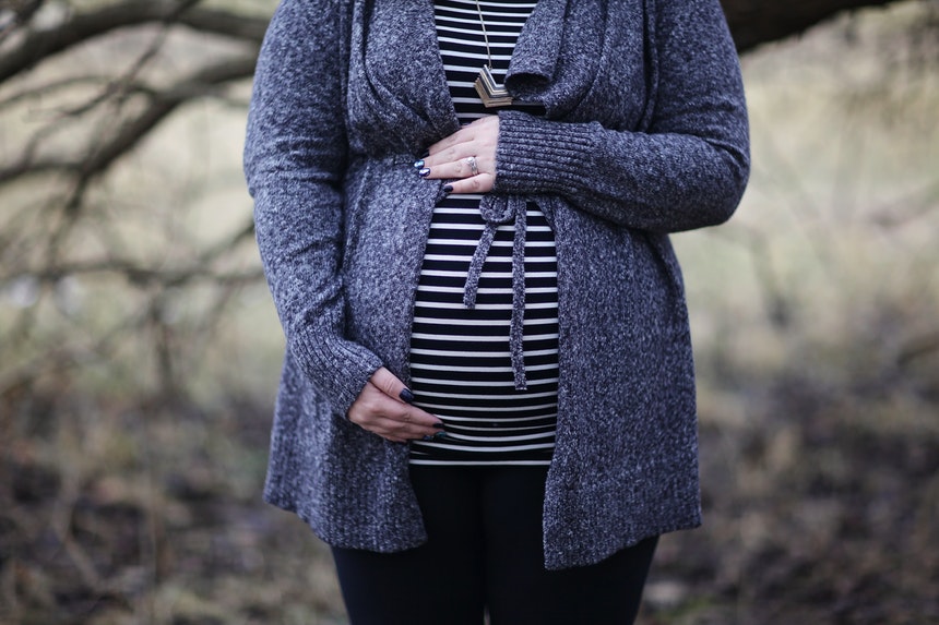 A pregnant woman wearing purple blazer holding her baby bump to celebrate pregnancy