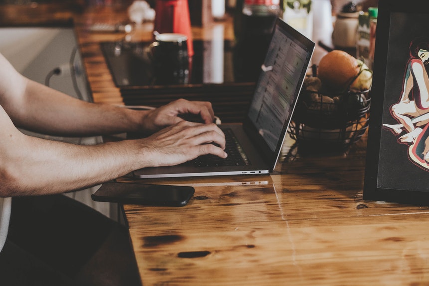 A man is writing an e-resume in his laptop placed on a wooden table