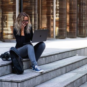 A woman sitting in a pavement while holding her laptop and phone in search for career success