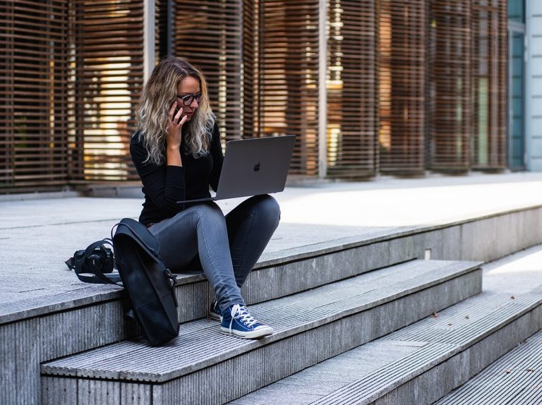 A woman sitting in a pavement while holding her laptop and phone in search for career success