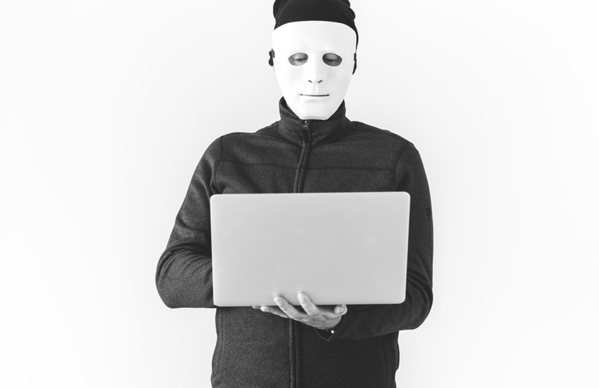 masked man holding a laptop while creating ripoff reviews