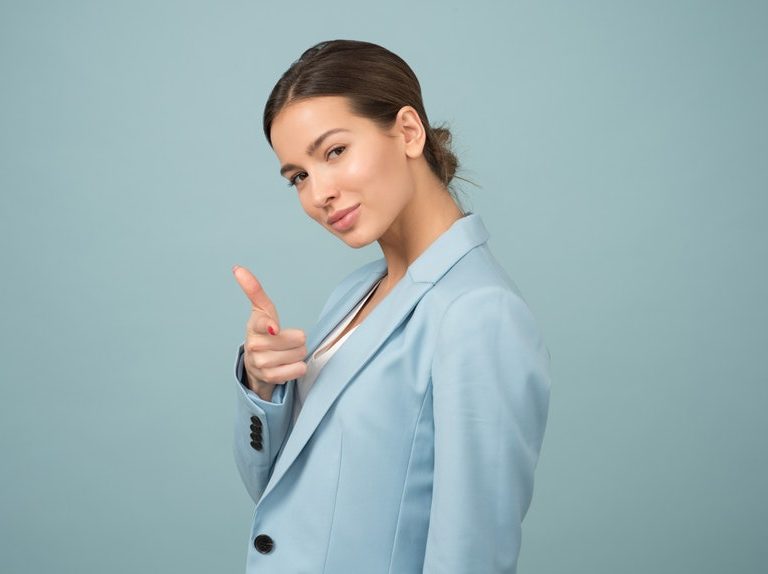 A productive career woman wearing a light colored blazer while pointing a finger gun to you