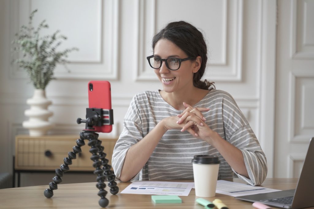 smiling woman sitting in front of smartphone on tripod shooting a video resume