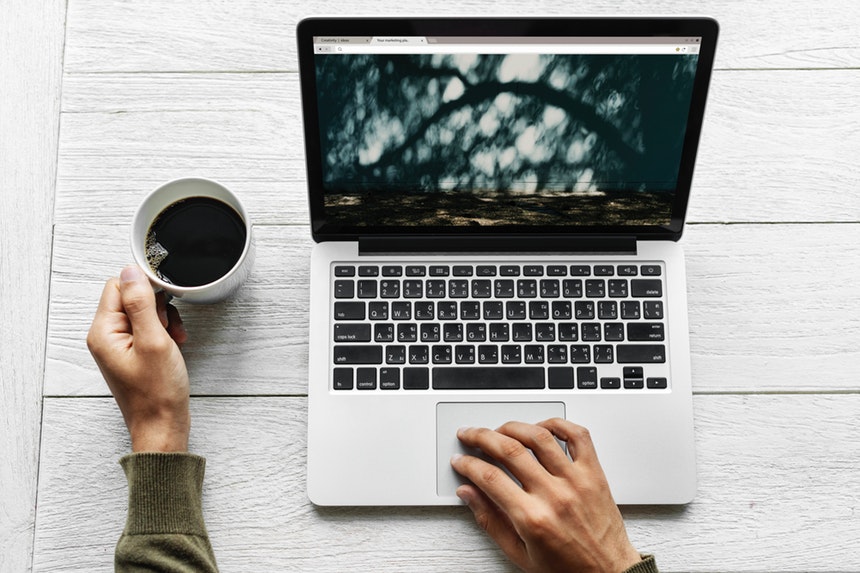 A man holding a cup of coffee in his left hand and typing in a laptop with his right hand