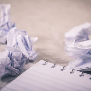 three crumpled paper with horrible resume mistakes written next to a notebook