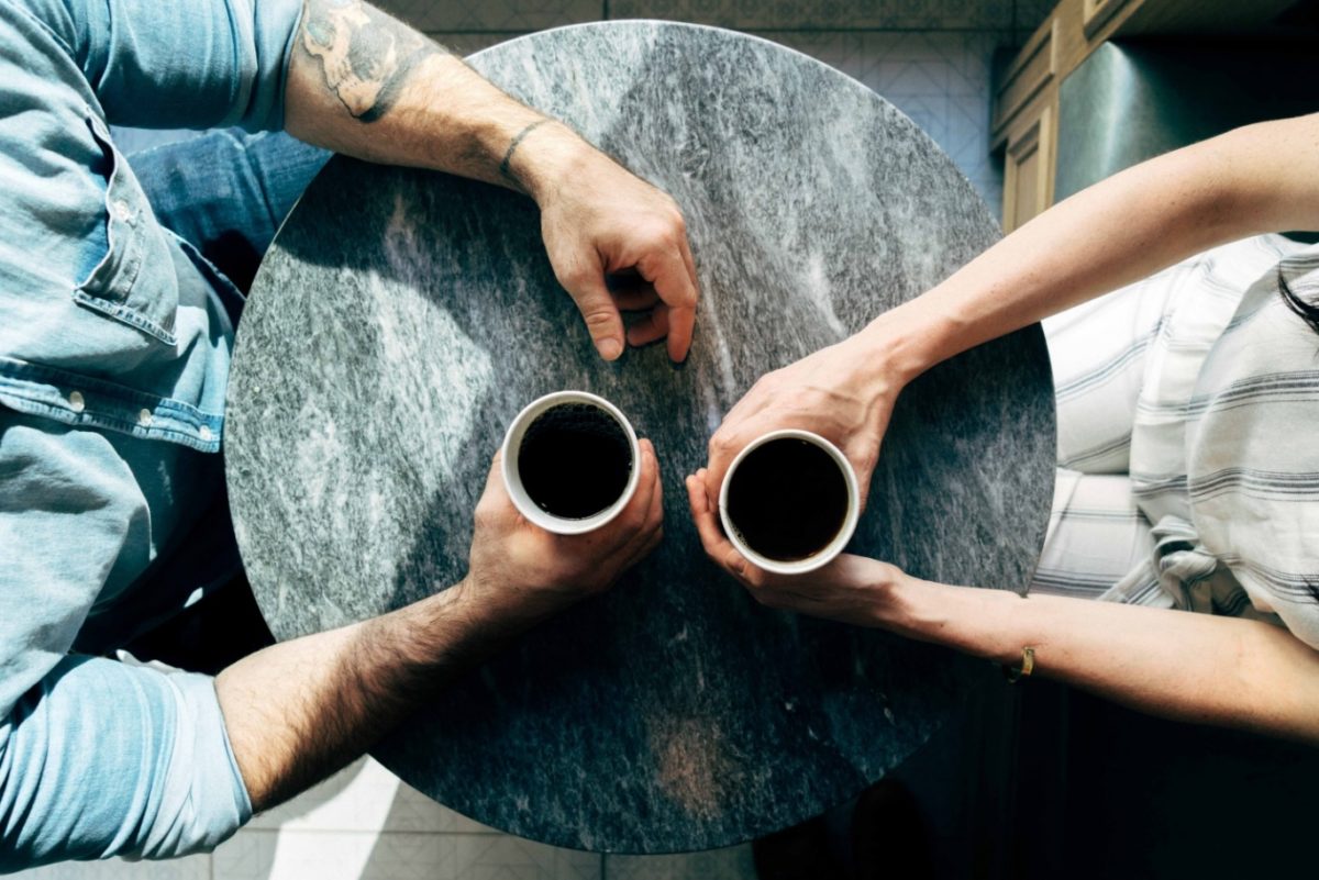 A man and a woman holding coffee and facing each other discussing several job interview stories with each other.