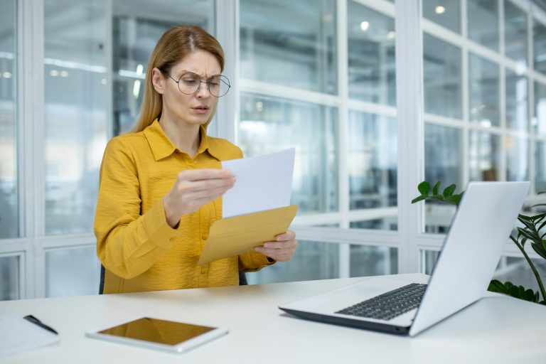 Businesswoman in yellow blazer reading a letter, expression of confusion and concern in office